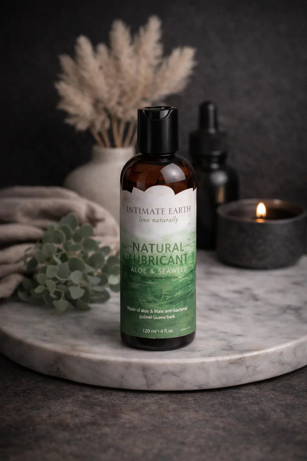 Intimate Earth natural lubricant bottle on marble tray with foliage, candle, and vase, Velore Wellness